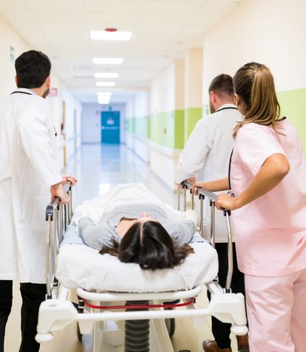 Doctors and nurse pushing female patient on stretcher at corridor in hospital