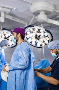 Medical professionals prepare for surgery in a sterile operating room, illuminated by bright surgical lights.