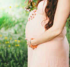Crop photo of pregnant woman with long dark hair on green bloom nature background